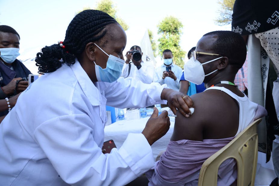 A healthcare worker administers an Oxford/AstraZeneca COVID-19 vaccine to her colleague