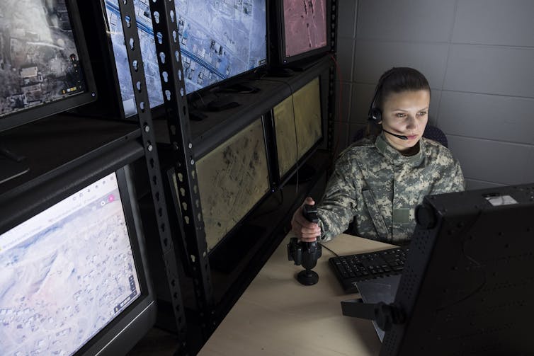 A women in military clothing controls a drone via a computer screen