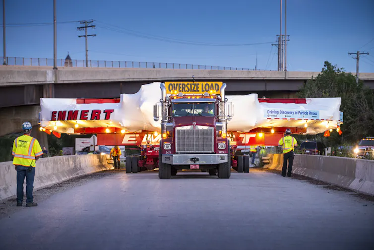 A truck carrying a much wider cargo down a road.