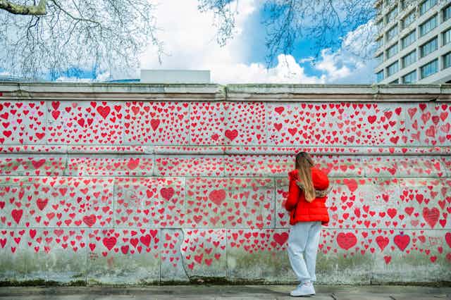 A visitor writes on a wall decorated with hearts in memory of the people who died of COVID-19 in the UK. 