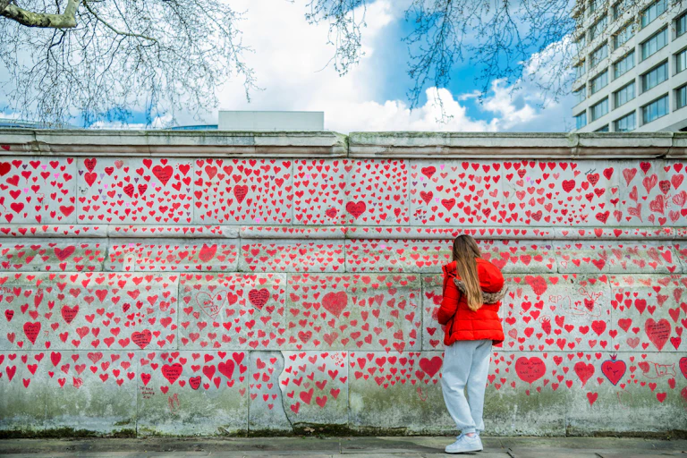 A visitor writes on a wall decorated with hearts in memory of the people who died of COVID-19 in the UK.