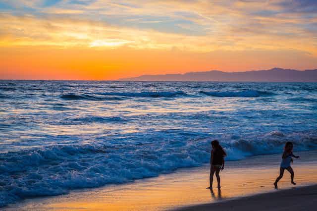 Children stand on the beach as the tide comes in at sunset.