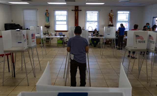 A voter fills out a ballot with Christ on the crucifix hanging on the wall in front of him.