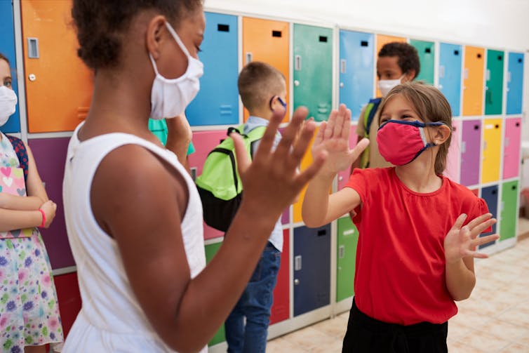 Two school girls wearing masks play together in a classroom.