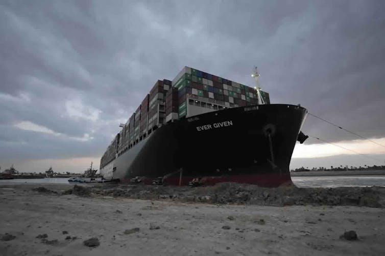 A large container ship known as the Ever Given is stuck in mud along the shore of the Suez Canal