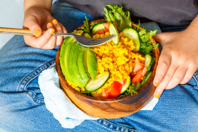 Bowl of rice and vegetables on lap of person holding a fork.