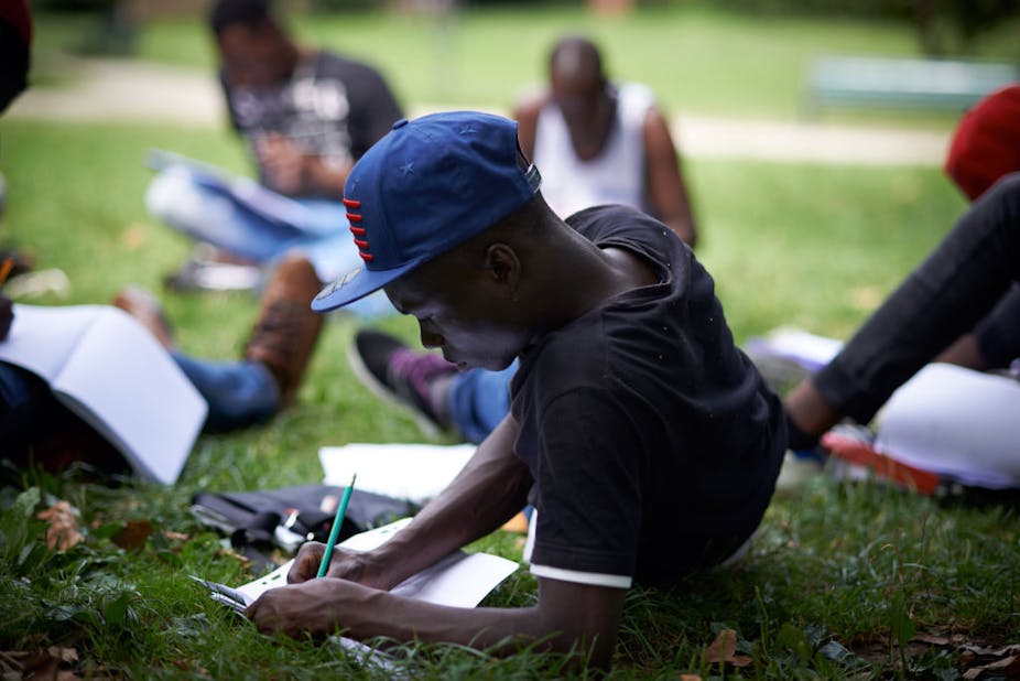 A young man writes in a book in a park