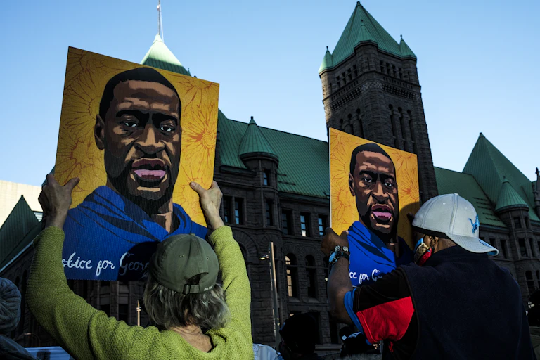 Two people putting up posters of George Floyd outside the government building in Minneapolis where Derek Chauvin's trial is being held.