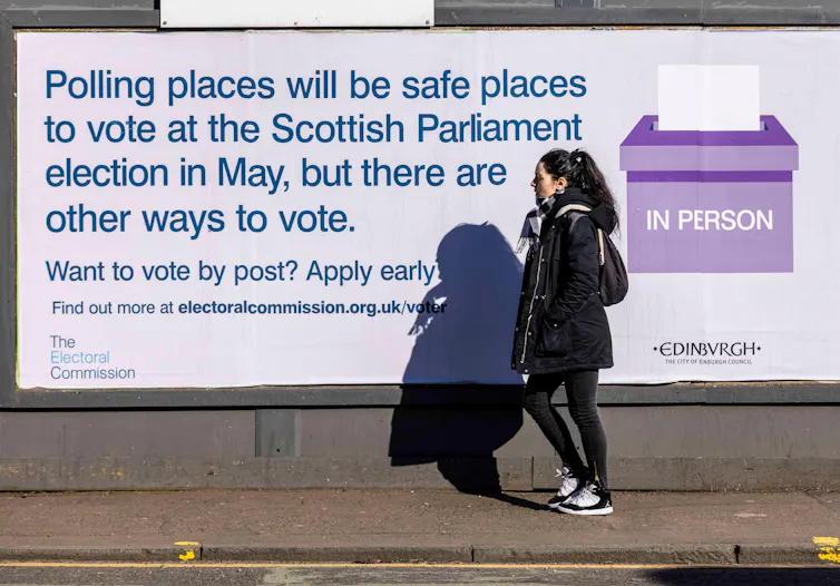 Woman walking past a poster about voting options for election