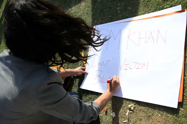 A Pakistani woman writes a sign in English protesting about Prime Minister Imran Khan's comments about violence against women.