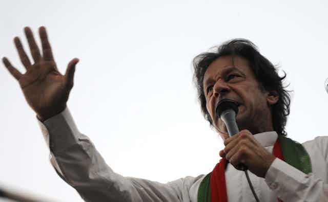 Pakistani prime minister, Imran Khan, in traditional dress, speaking into a microphone with his arm raised.