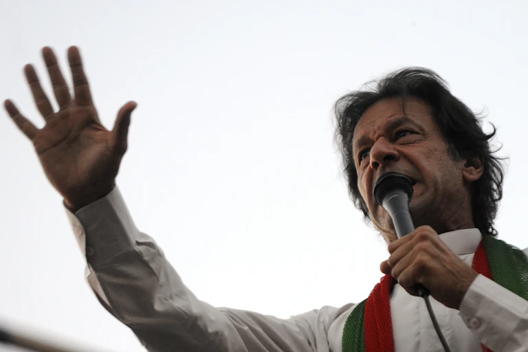 Pakistani prime minister, Imran Khan, in traditional dress, speaking into a microphone with his arm raised.