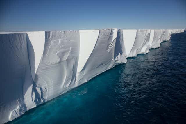 A towering ice shelf with deep-blue ocean water beneath.
