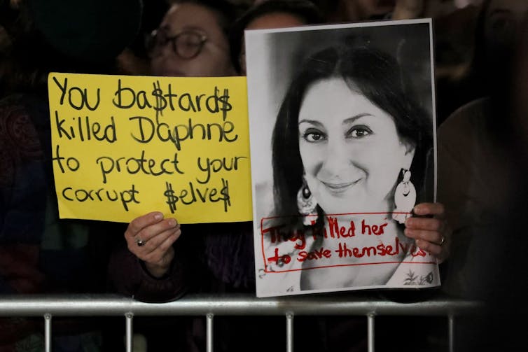 A woman holds up signs protesting the murder of Maltese investigative journalist Daphne Caruana Galizia.
