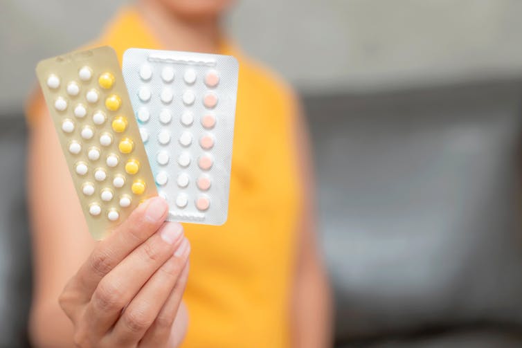 Une femme tenant deux plaquettes alvéolées de pilules contraceptives orales