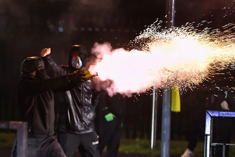 A young man shoots a firework during unrest in Belfast.