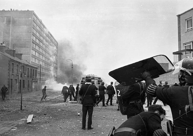 Black-and-white image of armed police occupying a smoky city street