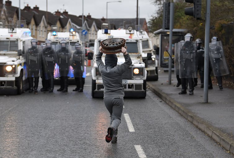 Protester throws a hubcap at police, who stand in a line wearing full riot gear