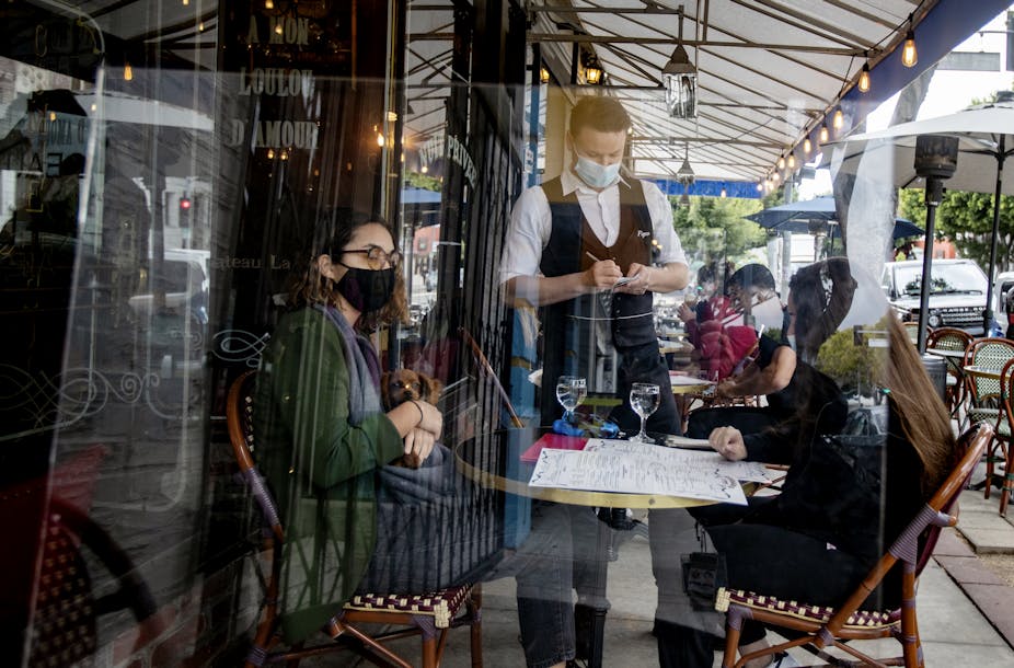 Waiter  takes food orders from customers behind a plexiglass at Figaro Bistro in Los Angeles County.