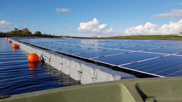 Floating solar panels mounted on plastic floats on a lake, with orange marker buoys.
