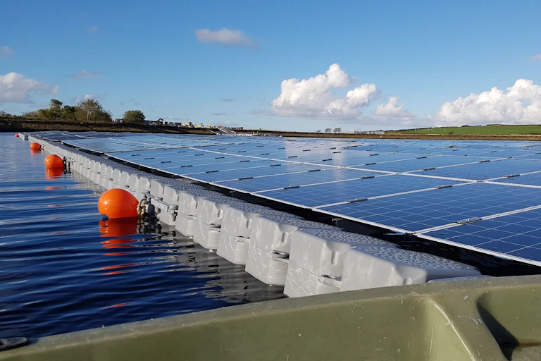 Floating solar panels mounted on plastic floats on a lake, with orange marker buoys.