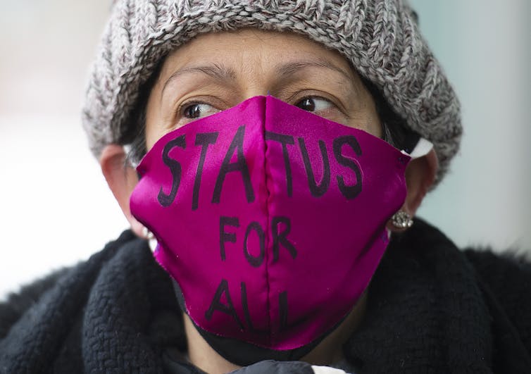 Woman wearing mask that reads 'status for all'