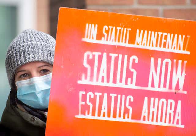 Woman holding sign that reads 'status now'
