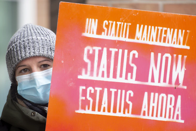 Woman holding sign that reads 'status now'