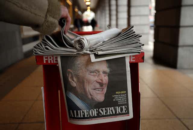 A man grabs a newspaper with a tribute to Prince Philip on the front page.