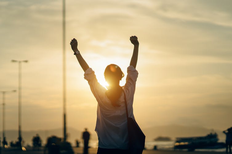 A silhouette of a young woman stretching her arms over her head in front of a sunset.