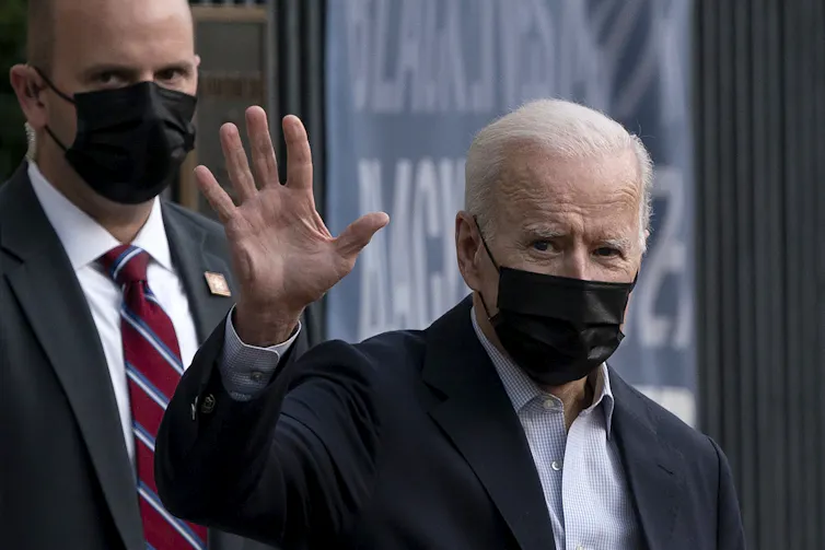 Joe Biden waves and wears a black mask