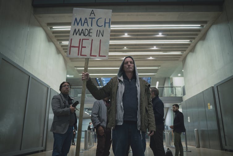 A man holds a sign: A Match Made In Hell