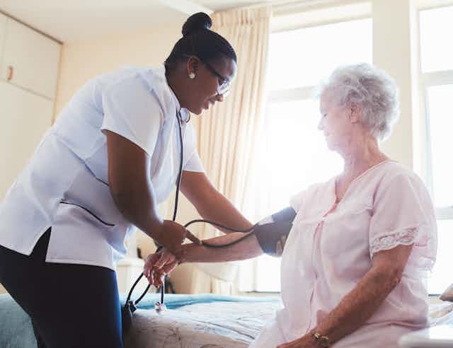 Female care worker check elderly woman's blood pressure.