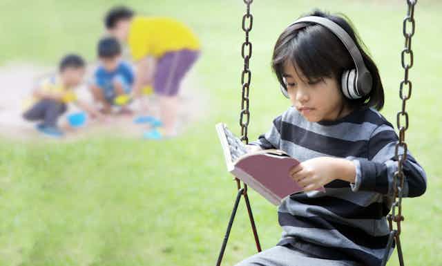 A girl wearing headphones on a swing in front of three children playing