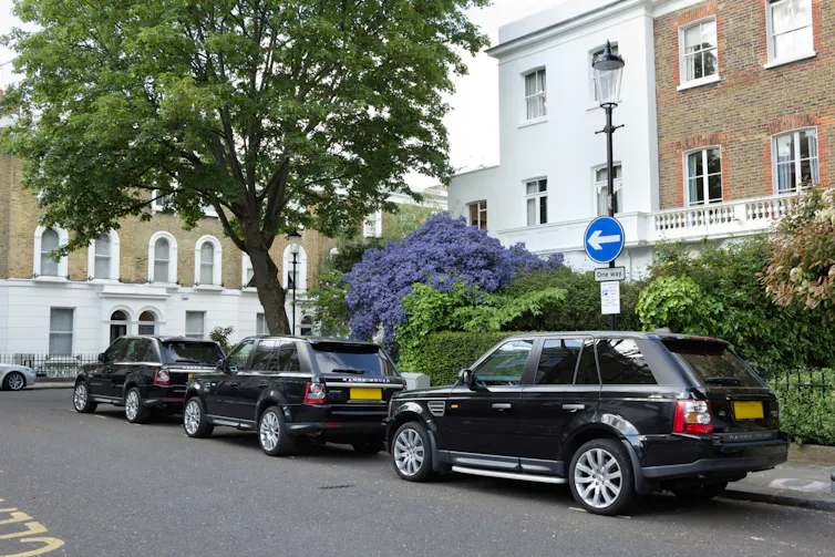 Three large, black SUVs parked in an affluent London street.