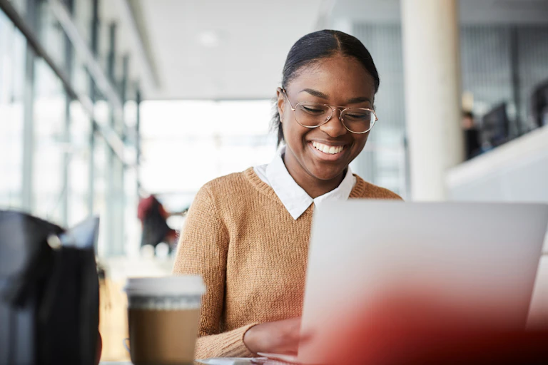 A college student smiles as she looks at the screen of her laptop computer.