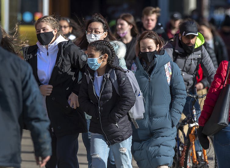 Pedestrians in face masks walk along a city street.