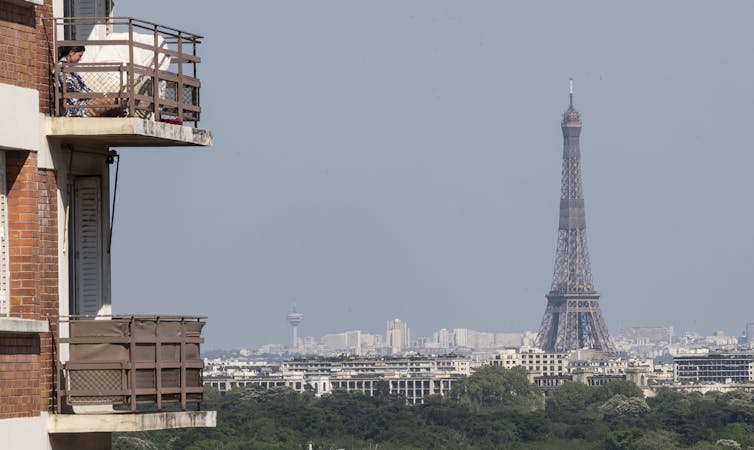 A woman enjoys the sun on her balcony as the Eiffel Tower is clearly seen in the background