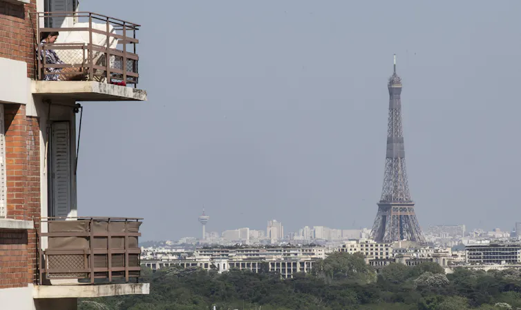 A woman enjoys the sun on her balcony as the Eiffel Tower is clearly seen in the background