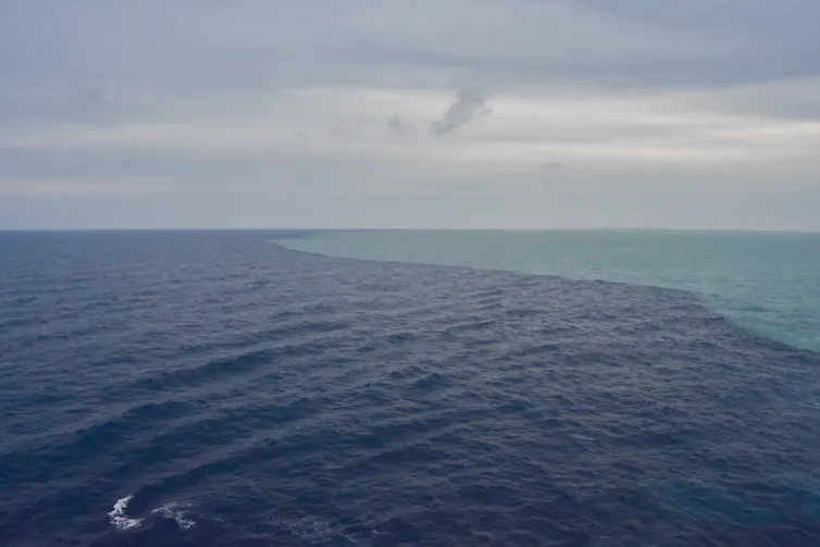 Dark blue water meets light blue water under a cloudy sky.