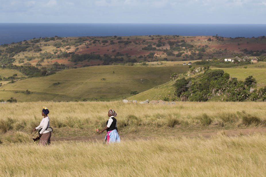 Two women walk one behind the other in a village in the Eastern Cape.