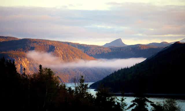Low clouds hang in fjord as the sun reflect on the surrounding hills.