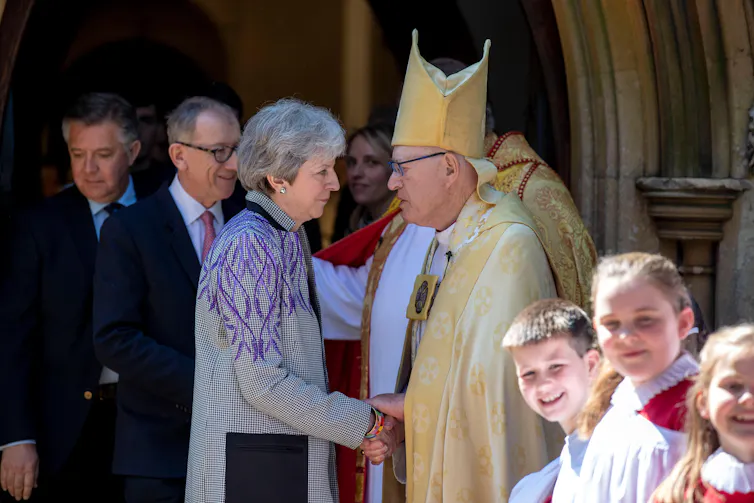 Theresa May shaking hands with an Anglican priest.