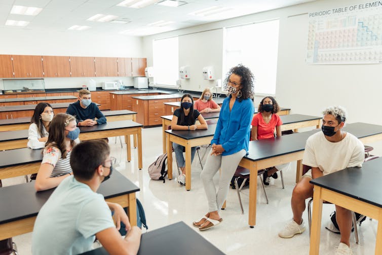 Students and their teacher sit around desks engaging themselves in a class discussion.