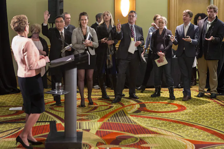 Reporters are lined up to ask questions of a politician standing at a lecturn