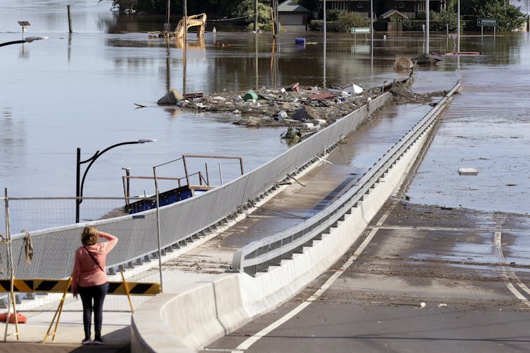 A woman looks at a bridge partially submerged in water