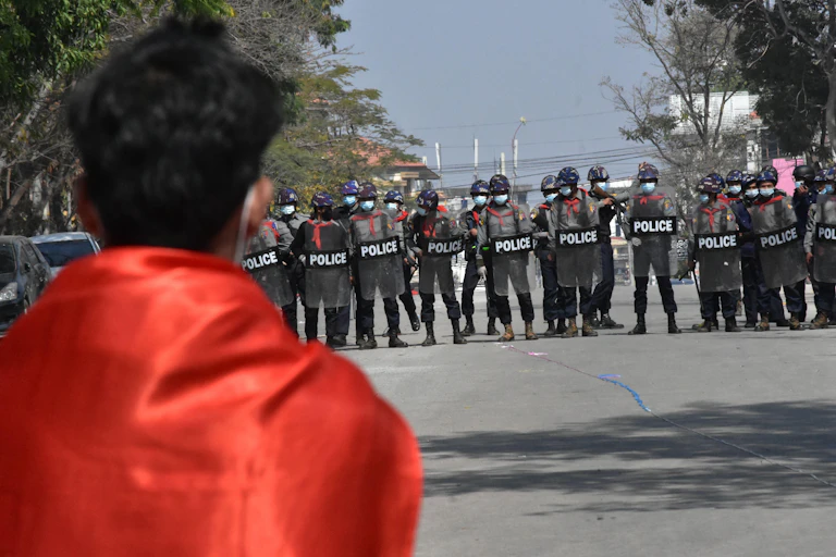 A protester watches as a line of police officers assembles wearing riot gear.