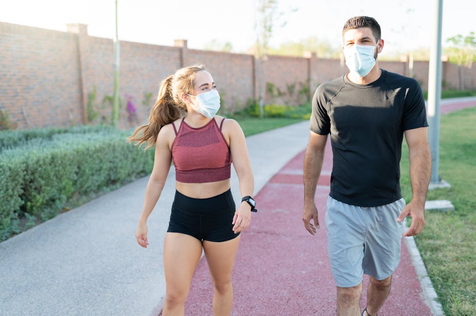 A young woman and young man walk outside in activewear while wearing face masks.