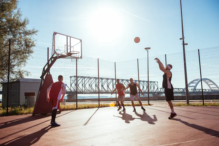 Five men play basketball outdoors.