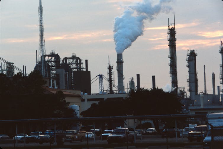 A factory with many stacks, one of which is emitting a cloud of smoke.